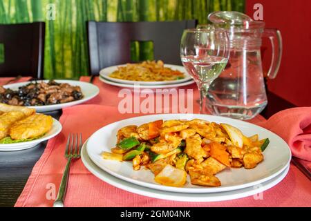 Chinesisches Rezept aus würzigem Chicken Wok mit Paprika, Zwiebeln, Zucchini, Karotten und Brokkoli auf dem Tisch eines Restaurants mit mehr chinesischen Gerichten Stockfoto