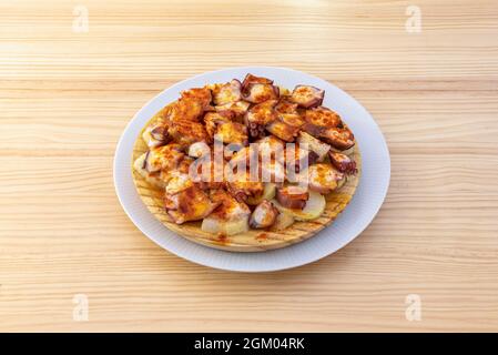 Köstlicher galizisch gekochter Oktopus auf einem Holzteller, der mit Paprika und Salz bestreut und mit Olivenöl auf einem Holztisch garniert wurde Stockfoto