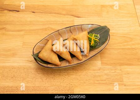 Tablett mit Gemüse Samosa in pakistanischen Restaurant auf Bananenblatt und Eichentisch gekocht Stockfoto