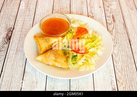 Gemüsesamosa mit Gewürzen, Eisbergsalat, Tomate und Dip-Sauce auf weißem Teller Stockfoto