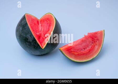 Wassermelone mit einer rot geschnittenen Scheibe ohne Samen auf blauem Hintergrund. Stockfoto