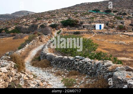 Pfad, der zum Aspropoumta Leuchtturm auf der griechischen Insel Folegandros führt, vorbei an landwirtschaftlichen Gebäuden Stockfoto