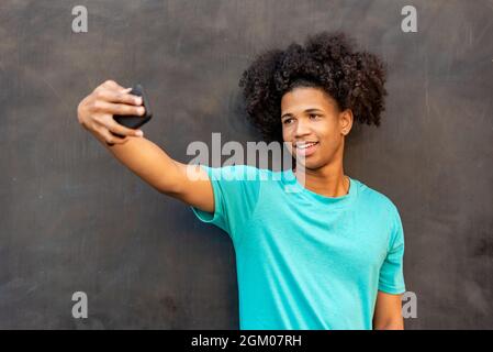 Afro-lateinischer junger Mann, der Selfie mit dem Handy gegen eine Wand nimmt Stockfoto