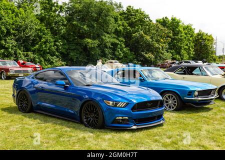 Ein moderner blauer Ford Mustang GT sitzt neben einem klassischen Mustang aus dem Jahr 1970, der die Entwicklung des Ponys auf einer Automobilausstellung in Fort Wayne, Indiana, USA, demonstriert. Stockfoto