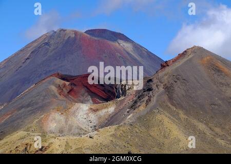 Leuchtend rote Vulkankrater und weit entfernte Wanderer auf dem Alpine Crossing im Tongariro National Park, North Island, Neuseeland Stockfoto