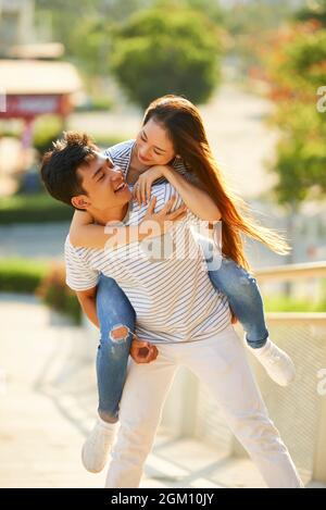Schöner, fröhlicher junger Mann, der seiner hübschen Freundin eine Huckepack-Fahrt gibt, wenn sie ein romantisches Date genießen Stockfoto