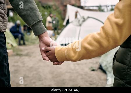 Rückansicht von nicht erkennbaren Kindern unterschiedlichen Alters, die sich beim Einziehen in das Migrantenlager die Hände hielten Stockfoto