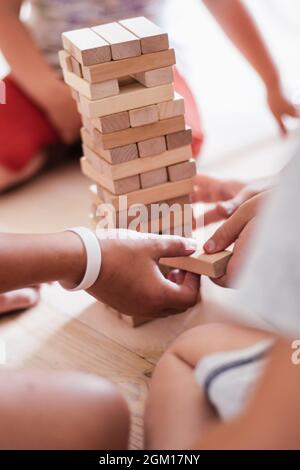 Verschwommene Kinderhände spielen Spiel mit Turm aus Holzblöcken. Vertikal Stockfoto