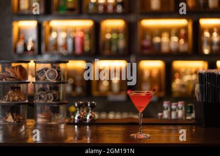 Nightlife-Konzept ein Glas rosa Champagner mit einer roten Kirsche auf der Oberseite, die auf einer Holzbar platziert wird, die sehr ansprechend aussieht. Stockfoto