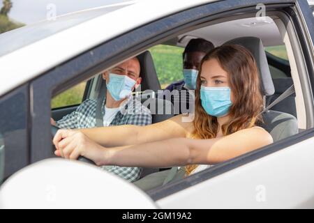 Junge Frau in Schutzmaske Auto mit Mitreisenden fahren Stockfoto