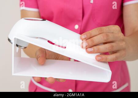 Medizinisches Personal in rosa Uniform hält Laser-Gerät für die Hautpflege von Gesicht und Körper. Jugend und Schönheit. Schönheitssalons. Kosmetologie. Dermatologie. Kosmetik Stockfoto