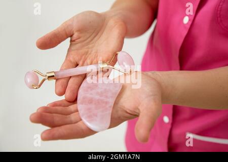 Kosmetologe in rosa medizinische Uniform hält Beauty-Tools für chinesische gua Sha Massage , aus natürlichen Rosenquarz . Jugend und Schönheit. Kosmetisches Mittel Stockfoto