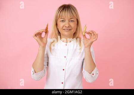 Die hübsche blonde Kosmetikerin in weißer medizinischer Uniform hält Kapseln für kosmetische Eingriffe in den Händen. Kleinunternehmen. SPA-Salon. Kosmetikindustrie. Stockfoto