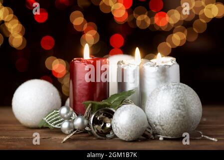 Brennende Weihnachtskerzen und Ornamente über verschwommenen festlichen Lichtern auf dunklem Hintergrund Stockfoto