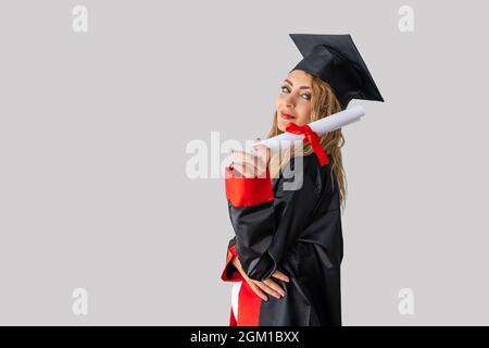 Eine hübsche Studentin, die ihren Abschluss feiert und vor einer weißen Wand steht und ihr Diplom mit Erfolg hält. Hochwertige Fotos Stockfoto