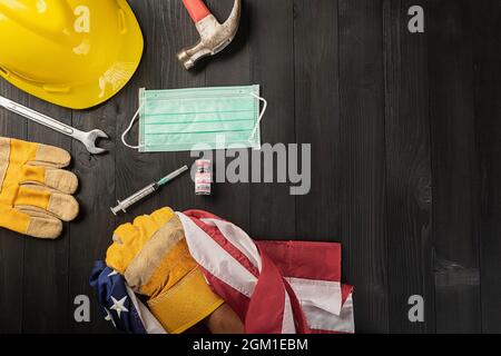 Happy Labor Day beim Ausbruch des Coronavirus. Mehrere Konstrukteurswerkzeuge, Handschuh mit ergreifender US-amerikanischer Flagge, Labor COVID-19-Impfstoff, medizinisch Stockfoto