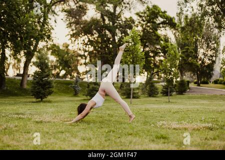 Die junge Frau in voller Länge praktiziert Yoga in nach unten gerichteter Hundehaltung, wobei ein Bein in der Natur im Park angehoben wird, Konzept der Wiederherstellung und Verlangsamung Stockfoto