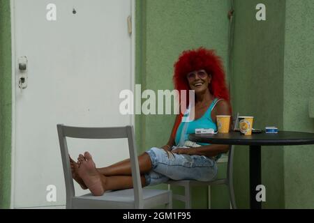 Tel Aviv, Israel - 20. August 2021: Ein Porträt einer rothaarigen Frau, die an einem grünen Haus in einer israelischen Straße in Tel Aviv sitzt. Stockfoto