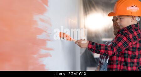 Profilansicht eines Jungen in einem Hut mit Papa, der die Wand im Zimmer in Orange malte. Die Familie macht Hausreparaturen. Männerarbeit und farbige Wand. Stockfoto