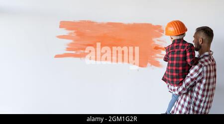 Renovierung in der Wohnung. Der Vater zog seinen Sohn auf, um die Wand mit einem Pinsel zu malen. Fröhliche Menschen renovieren ihr neues Zuhause. Stockfoto