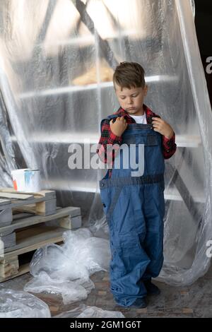 Junge Baumeister. Ein Kind in einem blauen Overall auf einer Baustelle. Anzug für den Baumeister. Stockfoto