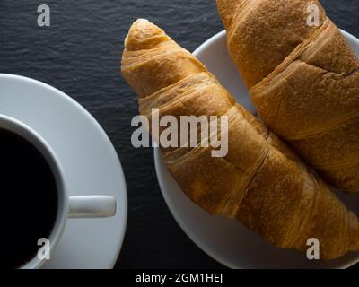 Tasse Kaffee und Croissants auf schwarzem Schieferhintergrund Stockfoto