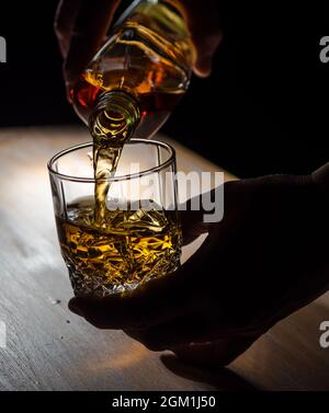 Whisky aus einer Flasche in ein Glas mit Eis gießen Würfel Stockfoto