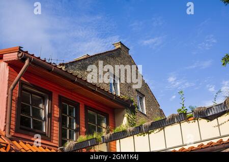 Abstrakte konzeptuelle Architektur von Vintage-Dächern aus Häusern mit Fenstern, Balkonen und Ofen und Lüftungsrohren vor blauem Himmel mit Wolken in der Altstadt. Wohnungen im Dachgeschoss gegen Skyline Stockfoto