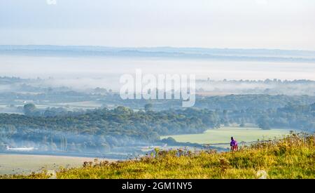 Brighton UK 16. September 2021 - ein Wanderer am frühen Morgen genießt die Mischung aus Sonnenschein und Nebel am Devils Dike entlang des South Downs Way nördlich von Brighton : Credit Simon Dack / Alamy Live News Stockfoto