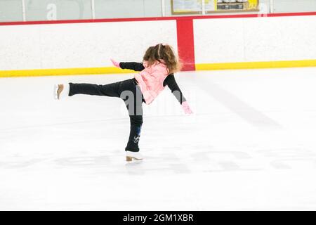 Kleine Mädchen, die Eiskunstlauf üben, bewegen sich auf der Indoor-Eisbahn. Stockfoto