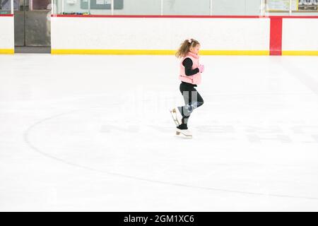 Kleine Mädchen, die Eiskunstlauf üben, bewegen sich auf der Indoor-Eisbahn. Stockfoto