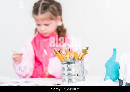 Homeschooling während COVID-19-Sperrung. Kleines Mädchen Malerei Papier mache Osterhasen Figur mit Acrylfarbe. Stockfoto