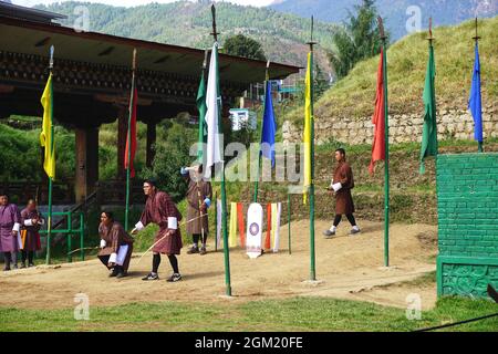 Bogenschützen aus Bhutan beobachten den Flug eines Pfeils zu seinem Ziel, das sich mehrere hundert Meter weiter auf dem Feld befindet. Bogenschießen ist der nationale Sport von Bhutan. Stockfoto