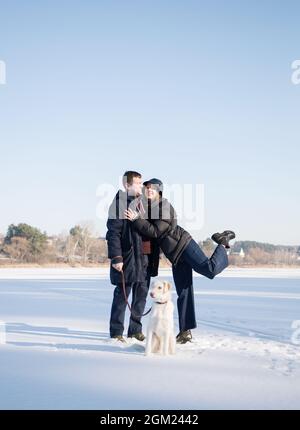 Verliebt glücklich Mann und Frau umarmen, gehen Sie den Hund im Schnee im Winter. Zarte Gefühle, festliche Stimmung, Freude der Beziehung. Valentinstag zusammen Stockfoto