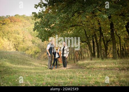 Fallen. Nahaufnahme einer glücklichen Familie im Hintergrund des Herbstwaldes. Glückliche Mutter, Vater und Sohn laufen im Wald und spielen. Stockfoto