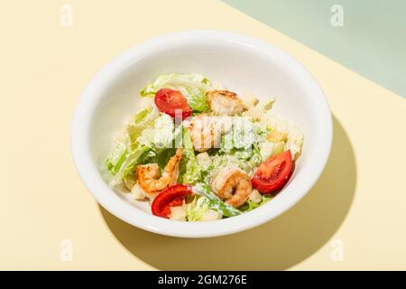 Caesar Salat mit Garnelen in weißen Teller auf gelb harten Schatten modern Stockfoto