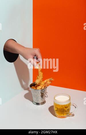 Frau Hand nimmt gebratene Garnelen in Metall Eimer durch Papier Loch modernen harten Schatten Bier Stockfoto