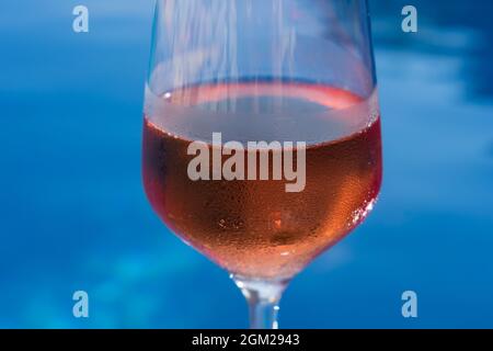 Nahaufnahme eines Weinglases, gefüllt mit Rosenwein am blauen Wasser für Feiern und Romantik Stockfoto