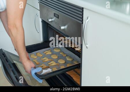 Frau nimmt ein Tablett mit frisch gebackenen Halloween-Keksen aus dem Ofen. Häusliches Leben. Speicherplatz kopieren. Stockfoto
