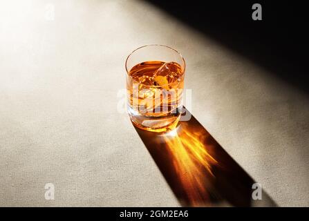 Ein Glas eleganter Whiskys mit Eiswürfeln an der Theke mit dunkler launischer Atmosphäre. Drink Art Konzept. Stockfoto