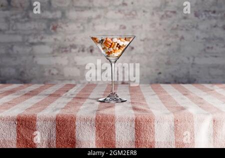 Martini-Glas gefüllt mit bunten medizinischen Pillen. Cocktail von Drogen, Drogenabhängigkeit oder medizinische Behandlung Konzept. Stockfoto