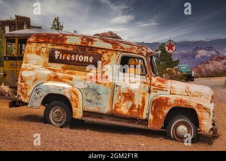 Firestone Truck - Ein alter verlassener und verwitterter Firestone Truck mit einer Texaco Tankstelle mit antikem Pick-up Truck im Hintergrund. Stockfoto