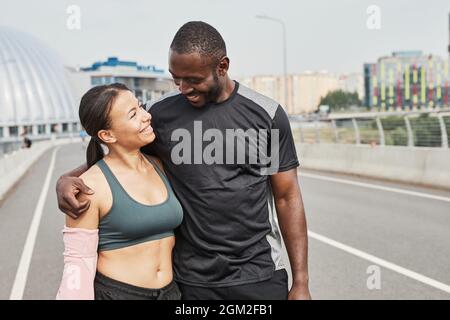 Afrikanisches junges Paar, das lächelt und sich umarmt, während es nach dem Training im Freien durch das Stadion geht Stockfoto