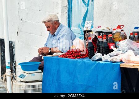 Juni 2021 - Sigacik, Izmir, Türkei: Älterer türkischer Bauer verkauft auf dem Bauernmarkt frisches Obst, Granatapfelsirup und Olivenöl in Flaschen. Stockfoto