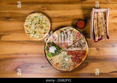 Verschiedene Pizzaarten kombiniert in einem mit Tomatensauce, Brotstäbchen und Pizzabrot Stockfoto