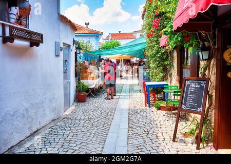 Juni 2021 - Seferihisar, Izmir, Türkei: Menschen, historische Gebäude und eine schmale Kopfsteinpflasterstraße in Seferihisar, Izmir, Türkei. Stockfoto