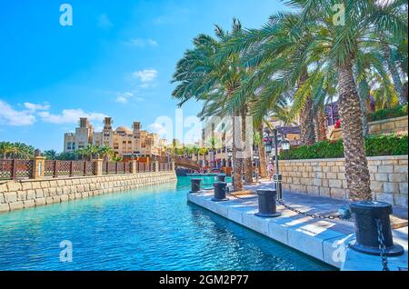 Die schattige Gasse entlang des Kanals des Souk Madinat Jumeirah Marktes, gesäumt von üppigen Palmen, öffnet den Blick auf das Souk-Gebäude im arabischen Stil mit barjeel W. Stockfoto