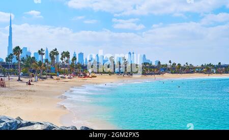La Mer Strandlinie mit Geschäften, Cafés, Palmenallee und der Silhouette des Burj Khalifa mit anderen Wolkenkratzern in der Innenstadt im Hintergrund, Dubai, VAE Stockfoto