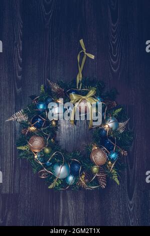 Handgefertigter, beleuchteter Weihnachtskranz mit hellgrünen blauen und beigen Dekorationen auf dunklem Holzhintergrund Stockfoto