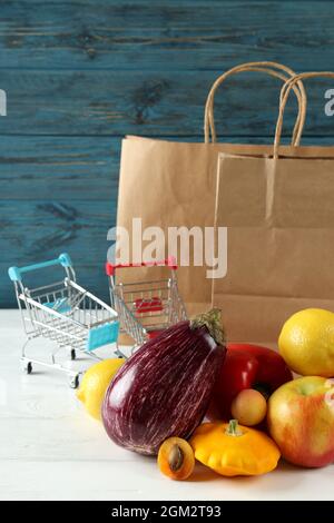 Papiertüten, Einkaufswagen, Gemüse und Obst auf Holztisch Stockfoto